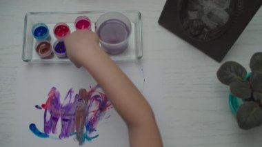 Çocuk elleri beyaz kağıt üzerinde çok renkli boyalar çiziyor. Çocuk parmağı resminin üst görünümü. 