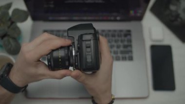 Erkeklerin elinde klasik fotoğraf makinesi. Adam lensleri çıkarıp peçeteyle siliyor. Masasında aletler olan üst görünüm. 