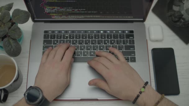 Le mani degli uomini che codificano sul portatile. Codice di scorrimento uomo sullo schermo. Vista dall'alto di laptop, smartphone, auricolari e tazza di caffè sulla scrivania . — Video Stock