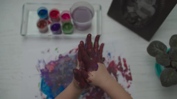 Gyerekek rajzolnak színes festékkel fehér papírlapra. Top nézet a gyermek ujj festés. — Stock videók