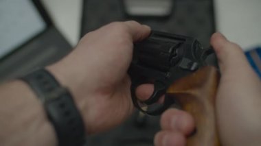Elinde tabanca olan bir adam onu temizliyor. Temizlikten önce erkek eller tabancayı test ediyor. Erkek masasının üst görüntüsünü kapat. 