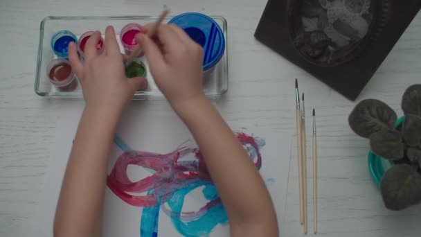 Kids hands drawing by multi-colored paints on white paper sheet. Top view of child brush painting. — Stock Video
