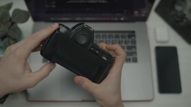 Vintage foto film kamera i manliga händer. Man vrider filmkameran i händerna, öppnar luckan. Ovanifrån med laptop på skrivbordet. — Stockvideo