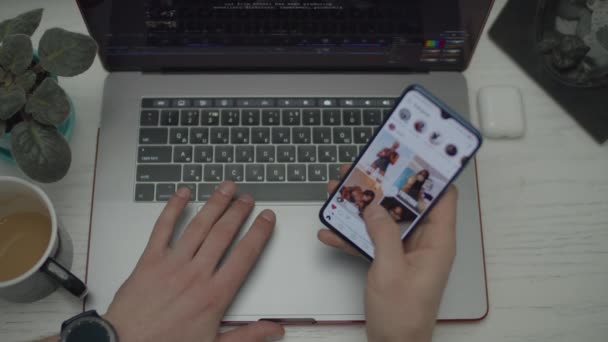 Mani da donna che lavorano al portatile. L'uomo scorre lo schermo del telefono prima. Vista dall'alto di laptop, smartphone, auricolari e tazza di caffè sulla scrivania . — Video Stock