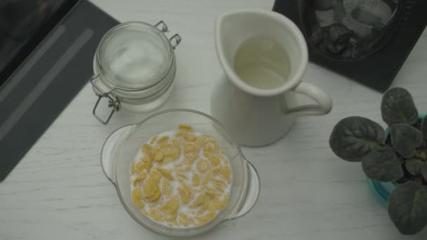 Glasschale mit Cornflakes mit Milch auf dem Arbeitstisch mit Tablet-Computer, Draufsicht. Hand essen Cornflakes mit Löffel. — Stockvideo