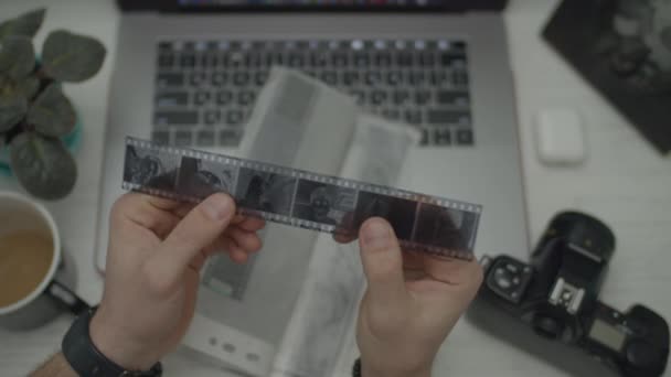 Photo negatives in male hands. Man holding black and white photo negatives. Top view with film camera and gadgets on desk. — Stock Video