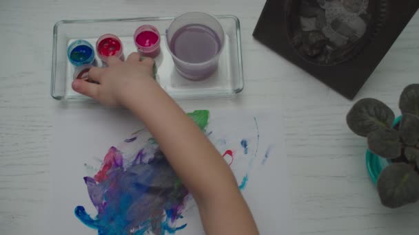 Kids hands drawing by multi-colored paints on white paper sheet. Top view of child finger painting. — Stock Video