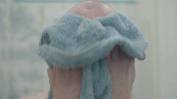 Homem barbudo careca a limpar a cara com uma toalha azul a olhar para a câmara. rotina matinal masculina no banheiro brilhante . — Vídeo de Stock