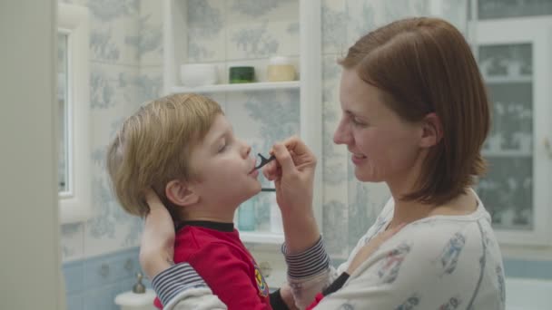 Young mother helps preschool boy in red pajamas with brushing teeth with dental floss. Fun family bath routine. Mother and son laughing in bathroom. — Stock Video