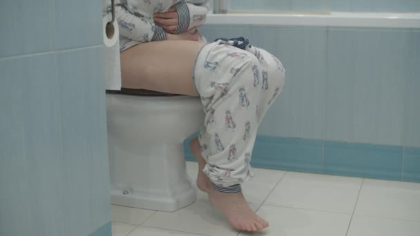 Vrouw in pyjama zittend op toilet in blauwe badkamer. Vrouw heeft maagproblemen, voelt pijn terwijl ze op het toilet zit. — Stockvideo