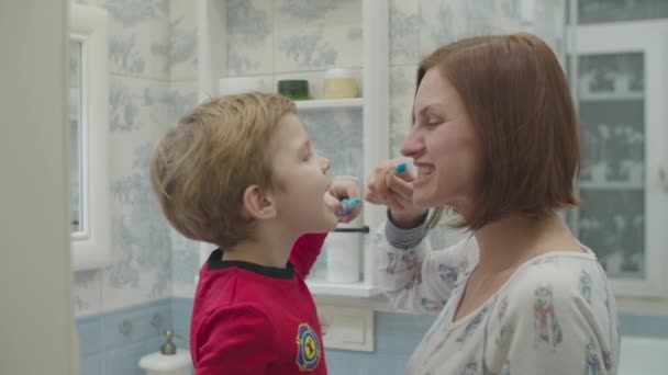 Young mother and preschool boy in red pajamas brushing their teeth. Fun family bath routine. Mother and son laughing in bathroom. — Stock Video