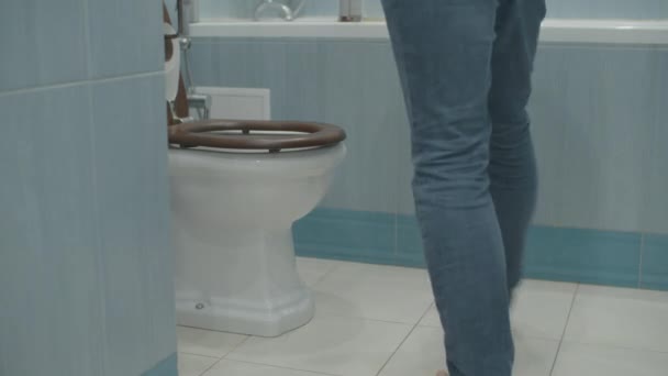Мужчина в джинсах приходит в белый туалет, снимает штаны и писает. Мужские ноги ходьба в ванной комнате . — стоковое видео