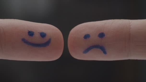 Dos dedos con emoticonos felices y tristes en las almohadillas de los dedos que se encuentran e interactúan. Felices emociones tristes en los signos. Vista macro . — Vídeos de Stock