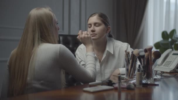 Dos compañeras solicitando maquillaje en la oficina. Visagiste aplica el maquillaje a la empresaria en el lugar de trabajo. Muchos cosméticos y pinceles en la mesa . — Vídeo de stock