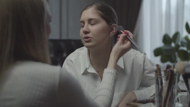 Twee vrouwelijke collega 's die solliciteren, maken het goed. Visagiste past make-up toe op zakenvrouw op het werk. Veel cosmetica en borstels op tafel. Sluiten.. — Stockvideo