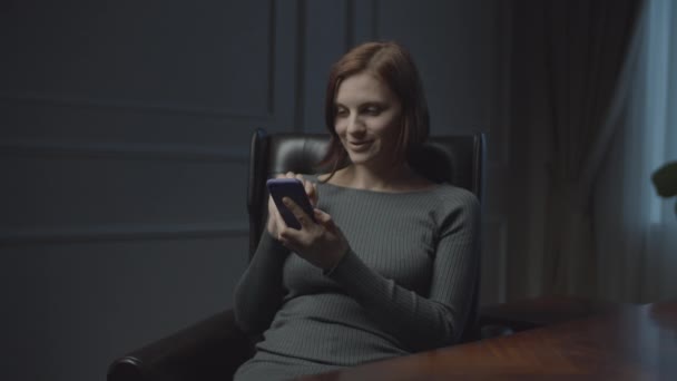 Young businesswoman working in business office at night. Woman surfing online in smartphone sitting in cozy office leather armchair. — Stock Video