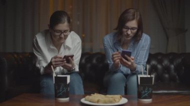 Gözlüklü, akıllı telefonlu, gülümseyen ve konuşan iki bayan gece geç saatlerde kanepede oturuyor. Sofrada yemek çubukları olan Asya yemekleri.. 