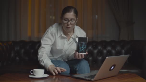 30-jährige Frau mit Brille, die asiatisches Kastenfutter mit Essstäbchen isst und auf den Laptop-Monitor blickt. spät einsam zu Hause Abendessen mit Gadgets. — Stockvideo