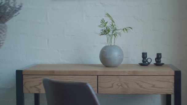 Mano mettendo vaso da fiori con lavanda secca sul tavolo spogliatoio con vaso da fiori rotondo e candelieri su di esso. Parete bianca e tavolo in legno . — Video Stock