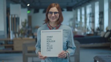 Young 30s brunette woman holding multilingual typescript welcoming text in white frame. Typewritten greeting text 