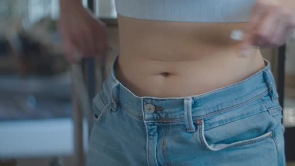 Young 30s woman measuring waist with centimeter tape. The result of weight loss in big size old jeans. — Stok video