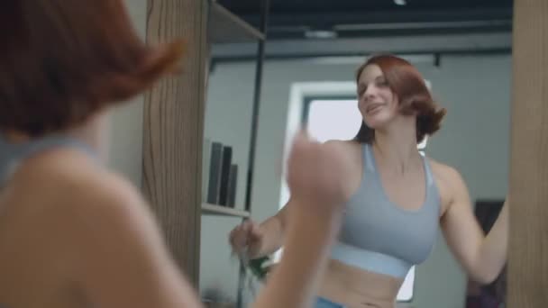 Young 30s woman admiring the result of weight loss while wearing big size old jeans. Happy female dancing in mirror with centimeter tape — Stok video