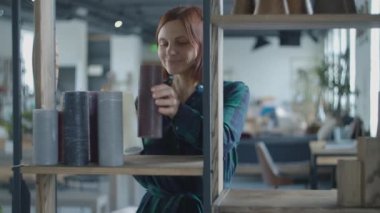 Happy dancing and singing into the candle like a microphone woman putting items at home to rights. Lilt female putting candles and pots to shelves. 