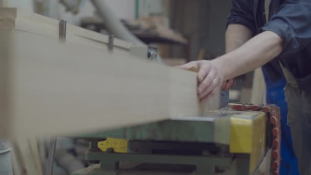 Manos masculinas de carpintero sosteniendo madera y llevándola a la máquina de carpintería. Procesos de taller de carpintería. Fabricación de muebles de madera — Vídeo de stock