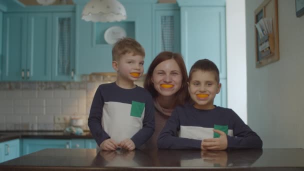 Divertida familia jugando con cáscaras de naranja en la boca. Mujer sonriente y niños con fruta naranja en la boca. Sonrisa naranja . — Vídeo de stock