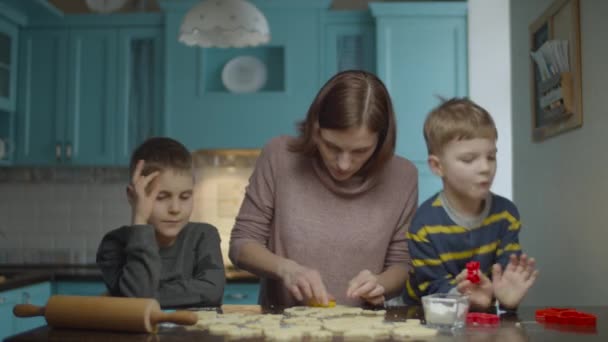 Young mother and two sons cooking different cookie shapes of dough. Kids helping mom to cook sweets on home blue kitchen. — Αρχείο Βίντεο
