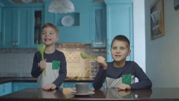 O familie fericită dansând și cântând în ustensile de bucătărie ca un microfon în bucătăria albastră domestică. Băieţii dansează în bucătărie. Scoop ca microfon . — Videoclip de stoc