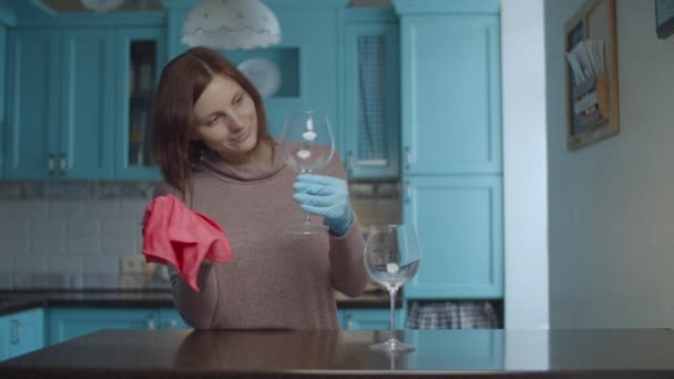 Joven mujer de 30 años sonriente con guantes limpiando vasos con servilleta rosa y bailando en la cocina azul. Mujer es feliz con la limpieza . — Vídeos de Stock