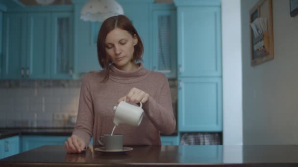 Joven mujer de 30 años que vierte leche de la olla en una taza de café. Mujer tomando una taza de café y oliendo. Café disfrutando proceso . — Vídeo de stock