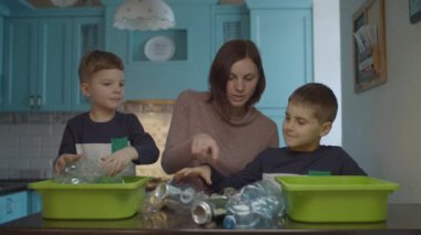 Young mother helping sons to sorting home garbage for recycling plastic and tin. Eco friendly family reducing plastic consumption. 