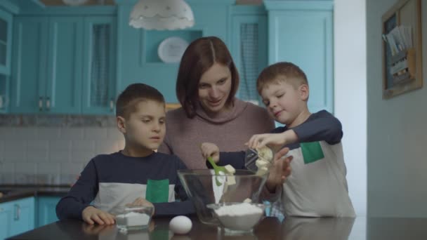 Kids helping mother to knead the dough of butter, sugar, egg and flour. Happy family cooking cookies and having fun on blue domestic kitchen. — Αρχείο Βίντεο