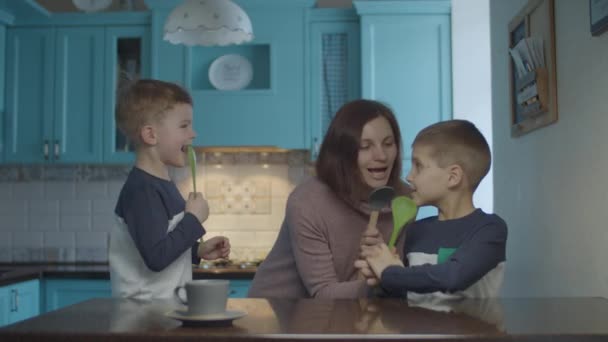 Feliz familia bailando y cantando en utensilios de cocina como un micrófono en la cocina azul doméstica. Mujer bailando emocional con niños en la cocina. Scoop como micrófono . — Vídeos de Stock