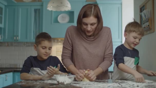 Щаслива сім'я розважається з борошном, готуючи печиво. Діти допомагають мамі замішувати тісто і грати з борошном на синій кухні . — стокове відео