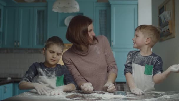 Famiglia felice divertirsi con la farina durante la cottura dei biscotti. I bambini aiutano la mamma a impastare l'impasto e a giocare con la farina sulla cucina blu . — Video Stock