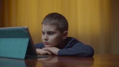 Masada oturan tablet bilgisayar kullanan otistik bir çocuğun portresi. Evde aletli otistik bir çocuk var. Otizm farkındalığı 