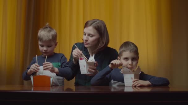 Matka z dwójką dzieci jedząca azjatyckie pudełko z pałeczkami w domu. Szczęśliwa rodzina jedząc obiad z pudełek dostawy. — Wideo stockowe