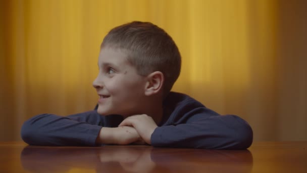 Egy autista fiú portréja, aki érzelmeket mutat az asztalnál ülve. Az autista kölyök vigyorog és nevetgél otthon. Autizmus tudatosság — Stock videók
