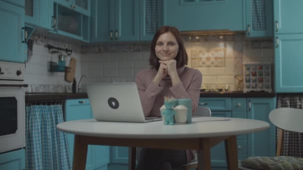 Giovane 30s femmina sorridente seduta al tavolo da pranzo con computer portatile su accogliente cucina blu. Ritratto di donna sorridente sulla cucina di casa . — Video Stock