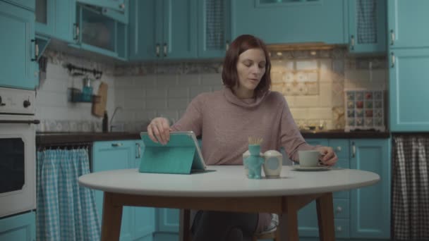 Jóvenes de 30 años hembra cansada de trabajar en casa, cerrando tableta y tomando una taza de café. Mujer haciendo pausa de trabajo para disfrutar de la bebida caliente en casa cocina azul . . — Vídeos de Stock