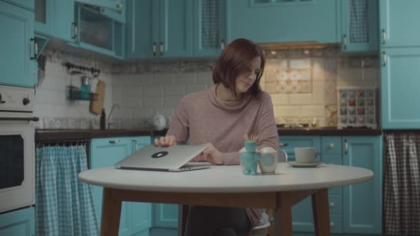 Giovane donna trentenne stanca di lavorare a casa, chiudendo il computer portatile e prendendo una tazza di caffè. Donna che fa pausa di lavoro per gustare bevanda calda a casa cucina blu . . — Video Stock