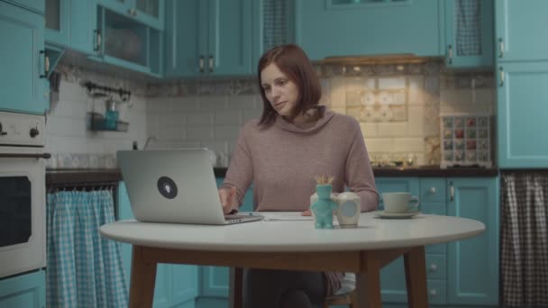 Třicátnice unavená prací v laptopu v kuchyni. Žena na volné noze doma pracovnice zavírající notebook, aby si odpočinula kvůli bolesti hlavy. Smutná pracující žena sedící u stolu. — Stock video
