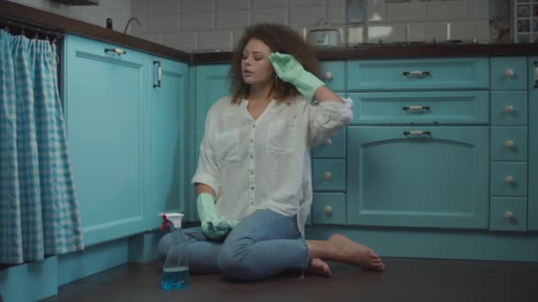 Young exhausted curly 20s female in cleaning gloves with rag tired of home clean up sitting on the floor and throwing away gloves. — Stock Video