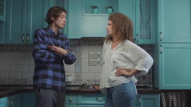 Молодая 20-летняя пара ссорится, стоя дома на голубой кухне, парень кричит, обвиняя девушку. Семейный конфликт . — стоковое видео