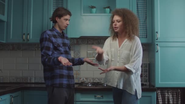 Mladý dvacetiletý pár se hádá doma na modré kuchyni, přítelkyně křičí obviňujícího přítele. Rodinný konflikt žárlivosti. — Stock video