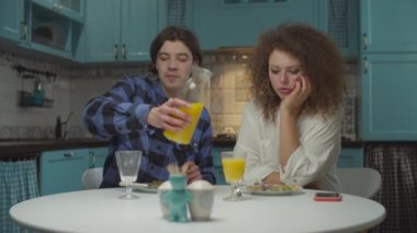 Genç mutlu 20 'li yaşlardaki çift rahat mavi mutfakta yemek yiyor. Adam, kız arkadaşına ağır çekimde portakal suyu dolduruyor.. 