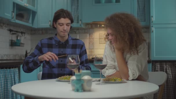 Young happy 20s couple in casual clothing having dinner with candle on cozy blue kitchen. Man trying to light the match for candle in funny way in slow motion. — Stock Video